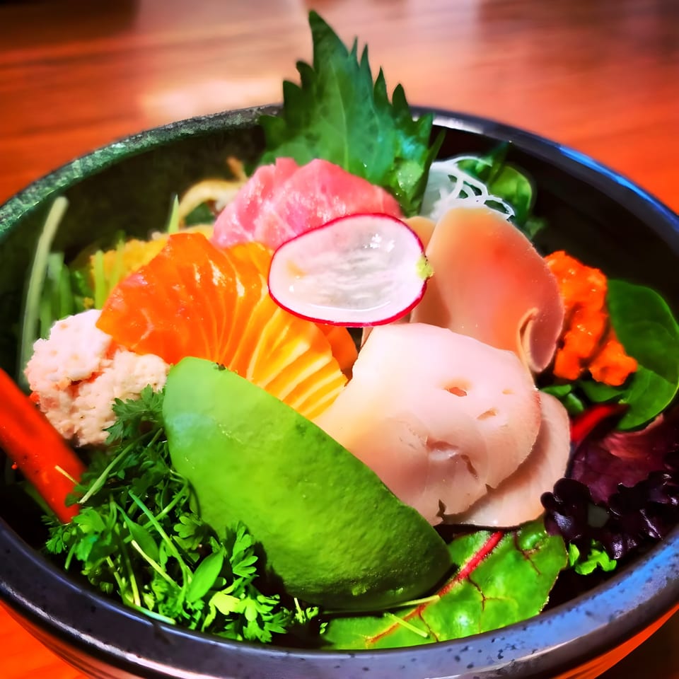 A colorful Sushi Goken chirashi bowl with various fish, avocado, radish, and greens.