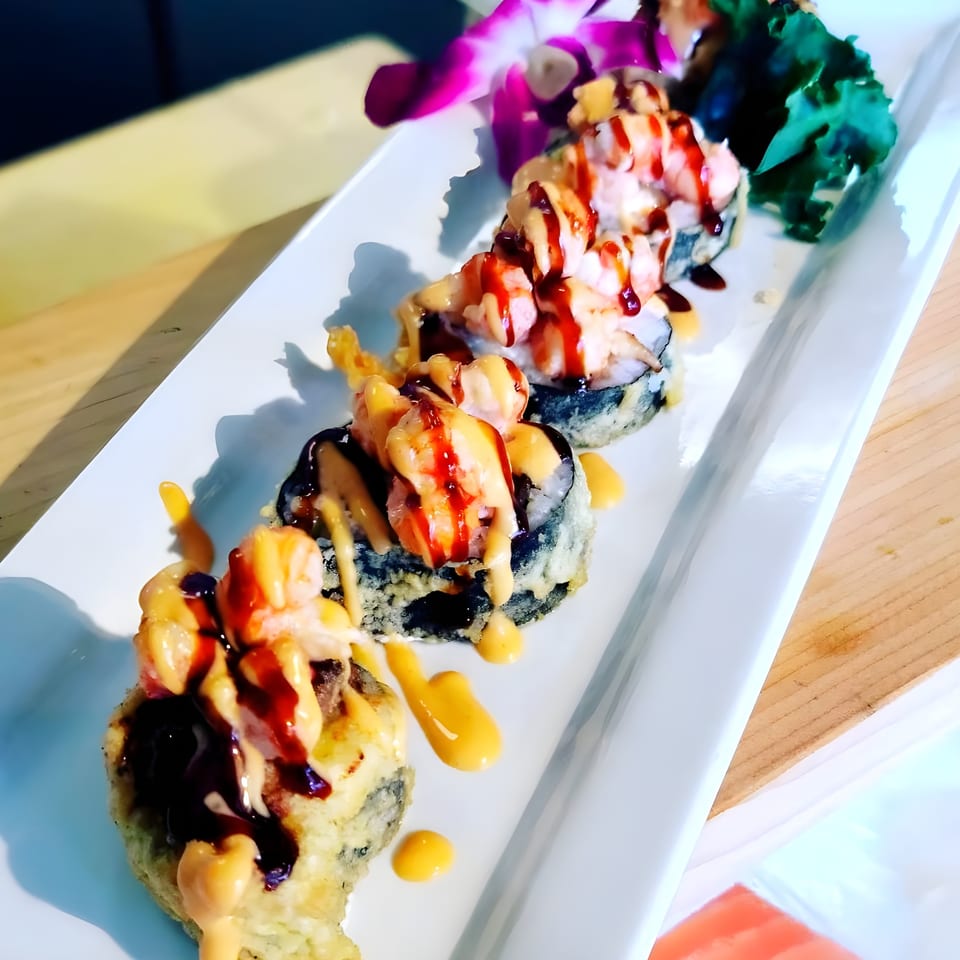 Sushi Goken's fried sushi rolls topped with shrimp, orange and brown sauces, and a purple orchid.